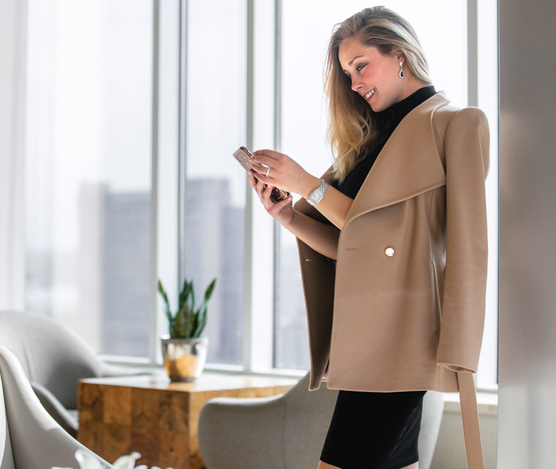 Professional businesswoman in luxury office building interior, with skyline in the window, holding smartphone